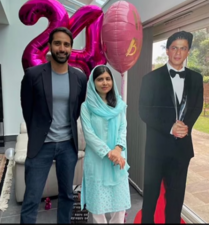 Malala and husband pose in front of Shahrukh Khan poster